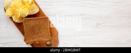 Homemade Peanut Butter Pickle Sandwich with Potato Chips on a rustic wooden board on a white wooden background, top view. Flat lay, overhead, from abo Stock Photo