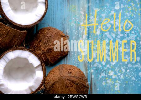 Hello summer. Greeting card with halves of coconuts on a blue wooden background. Stock Photo