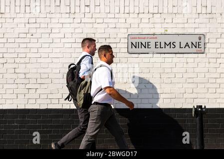 Two office workers walk past a Nine Elms Lane street sign in Lambeth, London, on a bright summer morning. Stock Photo