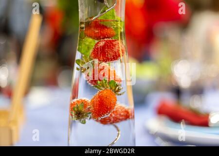 a carafe filled with water and strawberries stands on a served blue table. close up, soft focus. served table is on background in blur. Stock Photo