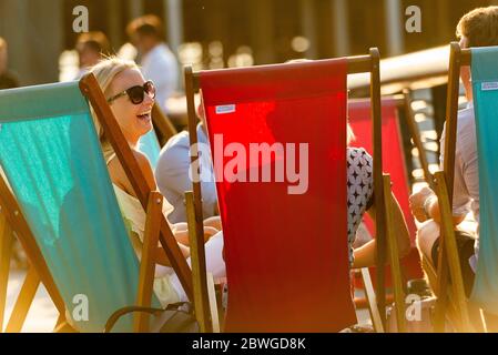 Young people drinking and socialising on a sunny summer evening near Battersea Power Station residential development. They look relaxed on deck chairs Stock Photo