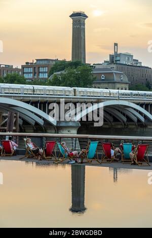 Friends socialise and relax in deck chairs on the Southbank of the Thames near Battersea Power Station redevelopment in the summer evening sun. Stock Photo