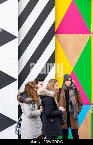Young people in winter coats stand in front of a bold, colourful mural in Battersea, London — a vibrant scene of urban youth and street art. Stock Photo