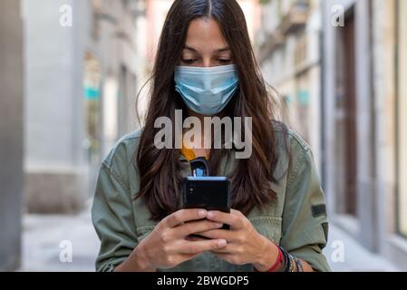 Woman wearing a protective mask on her face while using mobile phone in the street Stock Photo