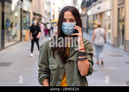 Woman wearing a protective mask on her face while using mobile phone in the street Stock Photo