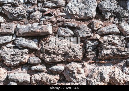 The texture of the wall of stones of different sizes, limestone, and shell rocks, concrete, and cement layers, shards of metal and bricks with clay Stock Photo