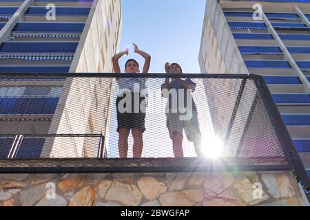 Kids clapping hands, applauding from terrace balcony to support doctors, nurses, hospital workers during Coronavirus Covid-19 pandemic quarantine Stock Photo