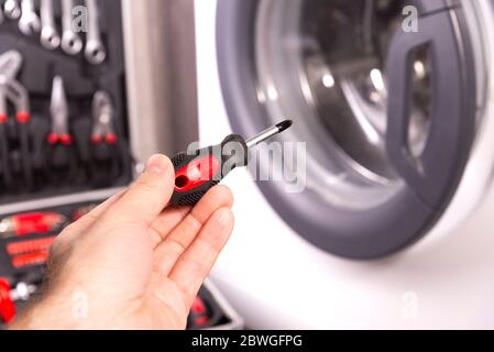 Repair and maintenance of the washing machine. Screwdriver in the hand of a master on the background of a washing machine Stock Photo
