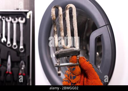 Repair of washing machines. Hand of a repairman with a turbulent electric heater covered with a coating of hard water. Replacing the electric heater Stock Photo