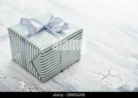 One striped  gift box with grey ribbon on white wooden background  closeup Stock Photo