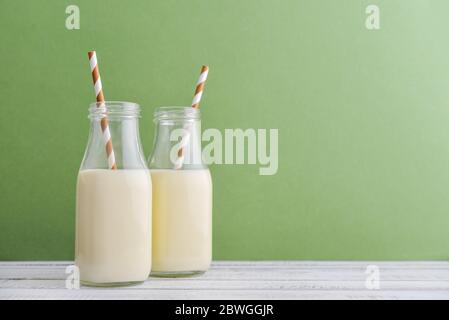 Two bottles with milk and drinking straws on green background Stock Photo