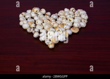 Makhana also know as lotus seeds are arranged or grouped in heart shape on brown wooden table shows health benefit towards heart Stock Photo