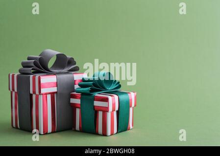 Two red striped gift boxes with green and grey ribbon on green background closeup Stock Photo