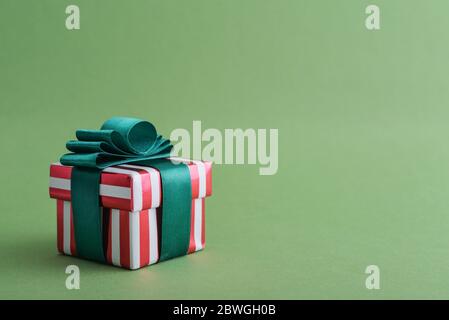 Red striped gift box with green ribbon on green background closeup Stock Photo