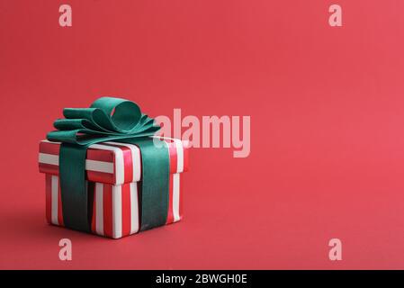 Red striped gift box with green ribbon on red background closeup Stock Photo