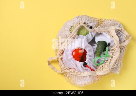 Tomatoes, cucumbers, cabbage in reusable mesh bags, in a large mesh bag on bright yellow background. Ecological concept. Stop pollution. Zero waste Stock Photo