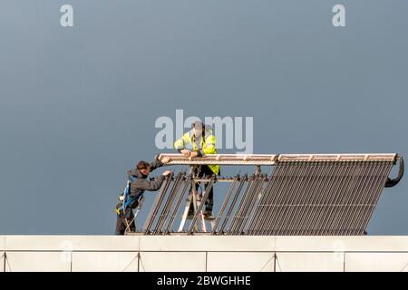 Technicians maintain photo voltaic solar panels on office building roof in Killarney Ireland as climate change concept. Stock Photo