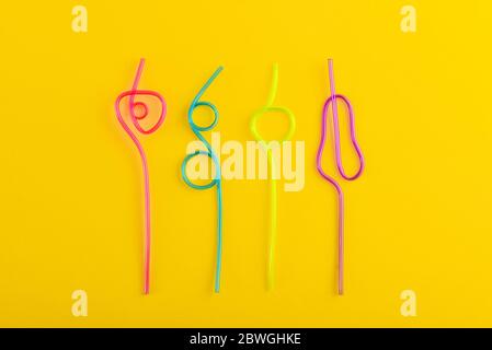 Multi-colored semi-transparent in many shapes straws. Drinking straws in the colors blue, purple, pink on a yellow background Stock Photo
