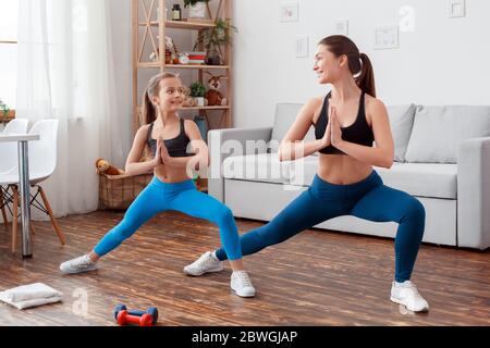 Smiling young adult woman and her little daughter making sport exercise together at home Stock Photo