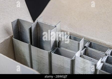 Staples for the office stapler in a cardboard container. Accessories for work in the office and at home. Dark background. Stock Photo