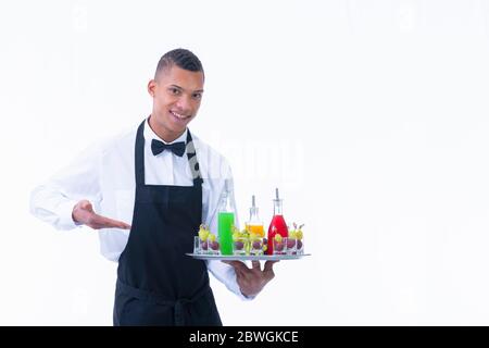 Handsome young waiter holding a tray with assorted liquor bottles and glass shots filled with grapes on a light background. Service and vegan cocktail Stock Photo