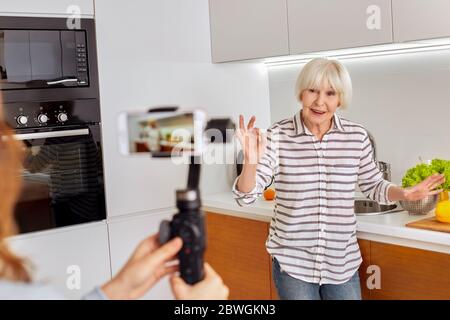 Mature aged woman and her daughter using modern smartphone, recording online video Stock Photo