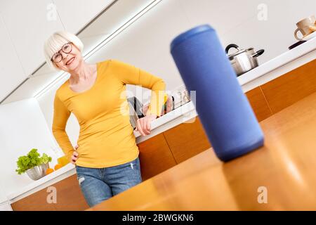 Mature aged woman using modern tablet computer and smart speaker Stock Photo