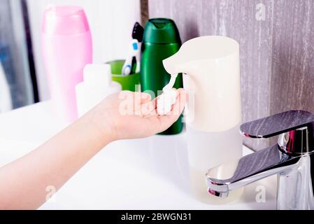 Hands collect liquid soap in a proximity sensor, near the sink with a tap in the bathroom Stock Photo