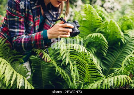 Young woman photographer taking photos on digital camera in summer park. Happy freelancer taking pictures of fern Stock Photo