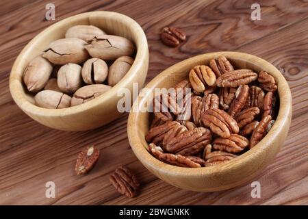 Peeled pecan nuts and unpeeled pecan nuts in bamboo bowls on wooden background Stock Photo
