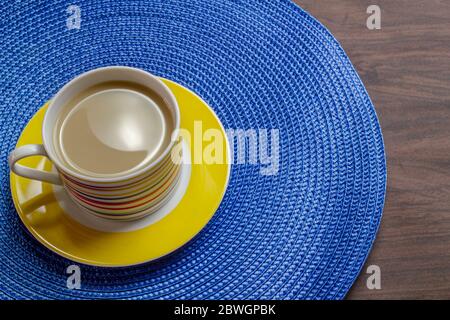 Coffee with milk in coloured mug on blue placemat and wooden table. Stock Photo