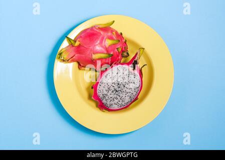 Cut dragon fruit in a yellow plate. Under pitaya with seeds on a colored background. Top view, flat layout Stock Photo