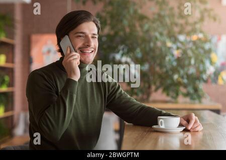 Smiling male entrepreneur talking to clients at cafe, using phone Stock Photo