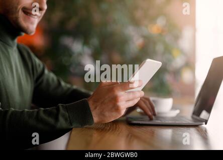 Young man holding smartphone and using laptop Stock Photo