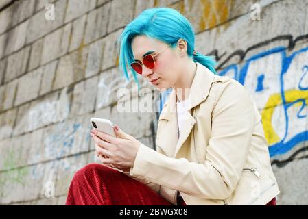 Kyiv, Ukraine - April 22, 2019: Beautiful young Caucasian girl with blue hair uses iPhone XS  outdoor Stock Photo
