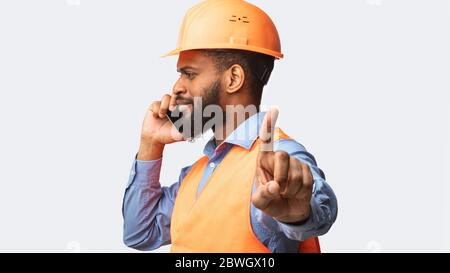 Construction Worker Talking On Cellphone Gesturing To Wait, White Background Stock Photo