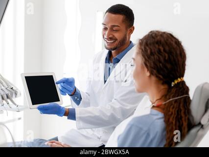 Smiling male dentist showing woman patient empty digital tablet screen Stock Photo