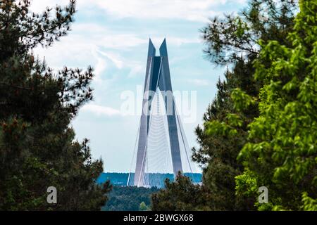 The view of hybrid cable-stayed, suspension bridge through the green trees with beautiful blue sky. Stock Photo