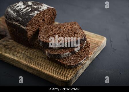 Wholegrain rye bread on a weathered wooden board on dark background Stock Photo