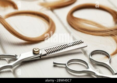 Cut hair curls and thinning scissors on a white wooden background. Stock Photo