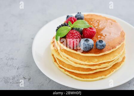 Pancakes with fresh berries and maple syrup on the  plate on grey background Stock Photo