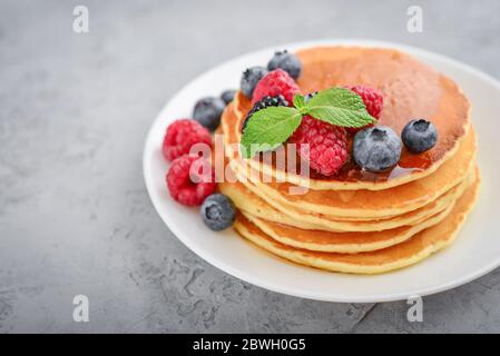 Pancakes with fresh berries and maple syrup on the  plate on grey background Stock Photo