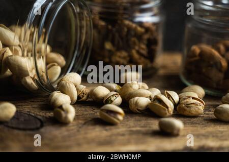 Pistachios scattered on the vintage table from a jar and with other nuts on background. Pistachio is a healthy vegetarian protein nutritious food Stock Photo