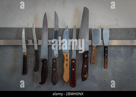 Collection of vintage kitchen knives on a magnetic holder on a white and grey wall Stock Photo