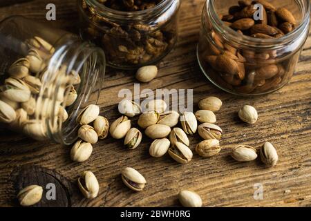 Pistachios scattered on the vintage table from a jar and with other nuts on background. Pistachio is a healthy vegetarian protein nutritious food Stock Photo