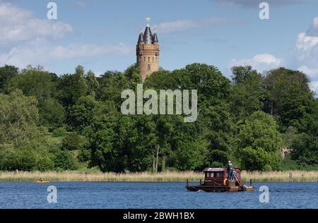 Potsdam, Germany. 28th May, 2020. The wooden raft 'Susi Harper' with the inscription 'Huckleberrys Flossstationen.de' sails on the Tiefen See past the Flatow Tower in Babelsberg Park. Credit: Soeren Stache/dpa-Zentralbild/ZB/dpa/Alamy Live News Stock Photo