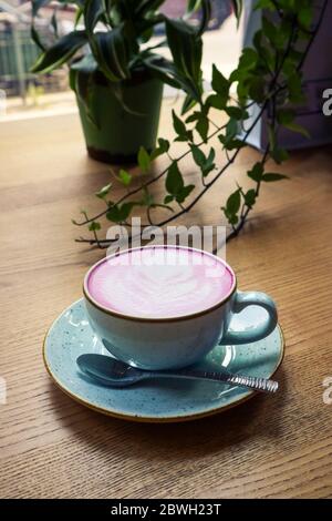 Cup of pink cappuccino in blue cup on wooden  table in a cafe closeup Stock Photo