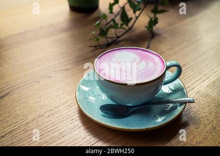 Cup of pink cappuccino in blue cup on wooden  table in a cafe closeup Stock Photo