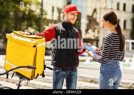 Girl Receiving Restaurant Food Order From Courier On Bike Outdoors Stock Photo