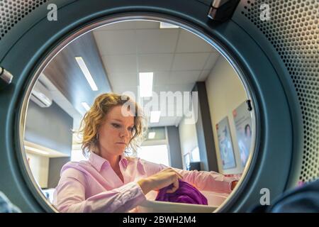 woman putting clothes in a dryer in a public laundry Stock Photo